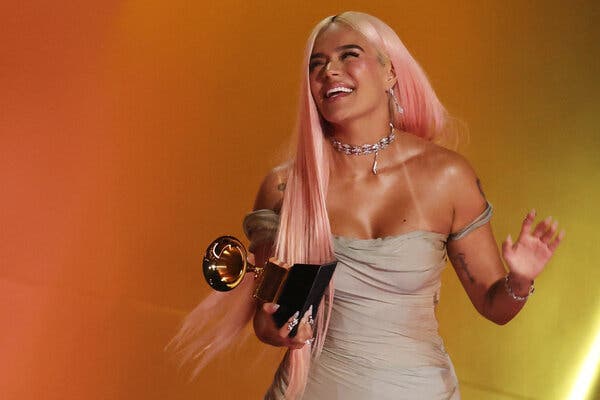 A woman with blond and pink hair smiles and holds a Grammy Award in a strapless tan dress.