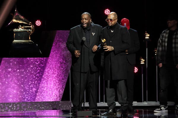 Two men dressed in black stand on an awards show stage accepting a trophy.