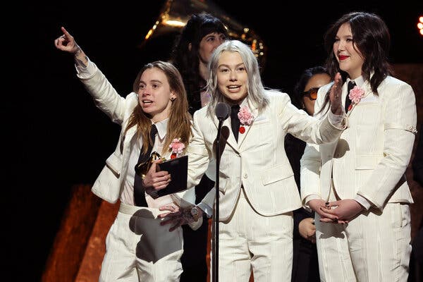 Three women in matching white suits stand at a microphone, accepting an award.